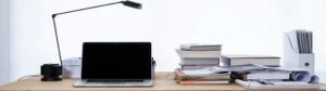laptop and stacks of books on desk with lamp